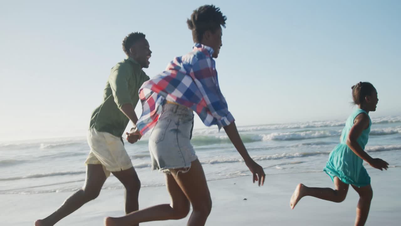 Happy african american couple running with daughter on sunny beach