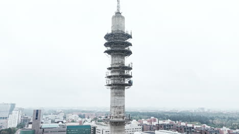 aerial approaching low angle shot of a bleak industrial concrete television and radio link tower in pasila, helsinki, finland on a bright and foggy day