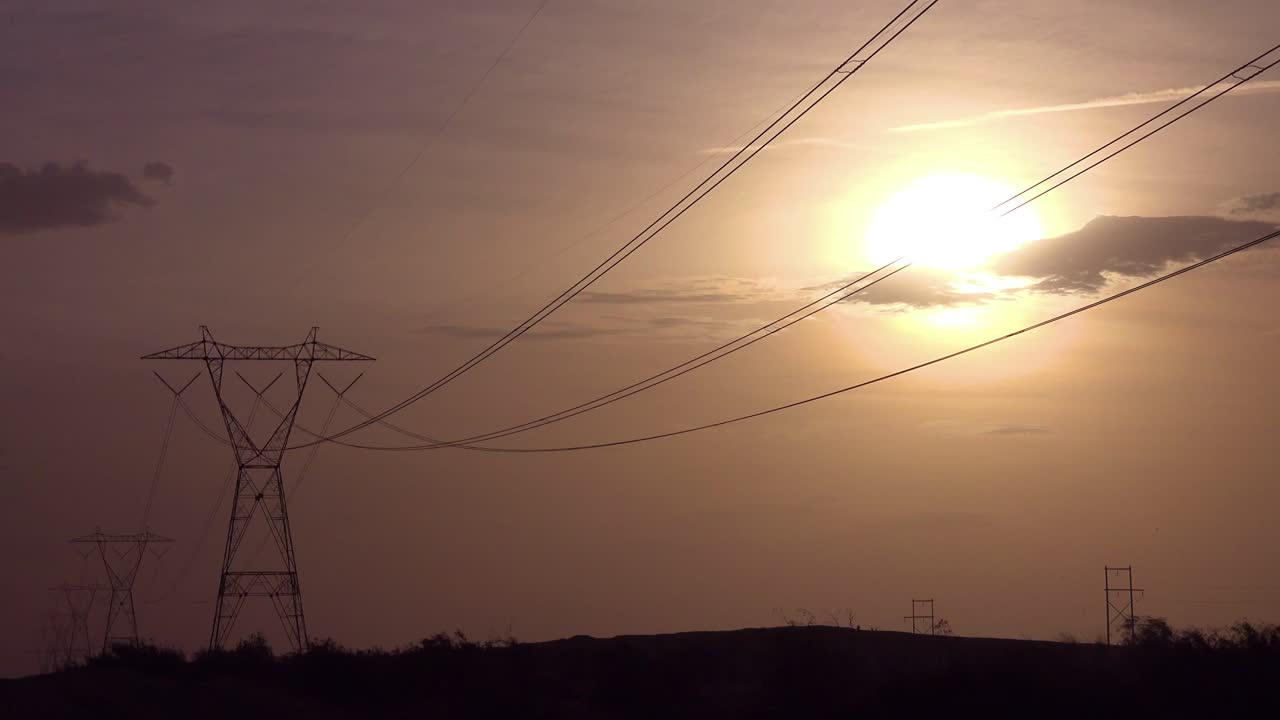 Energy power lines run across the desert against the sun