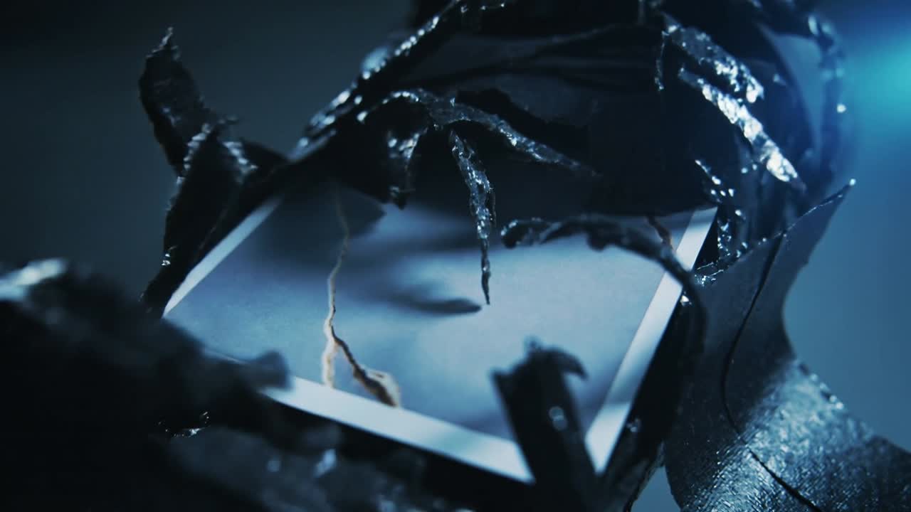 Camera focusing wrapped cylinder revealing glossy black film peeling in studio, with cracked panel