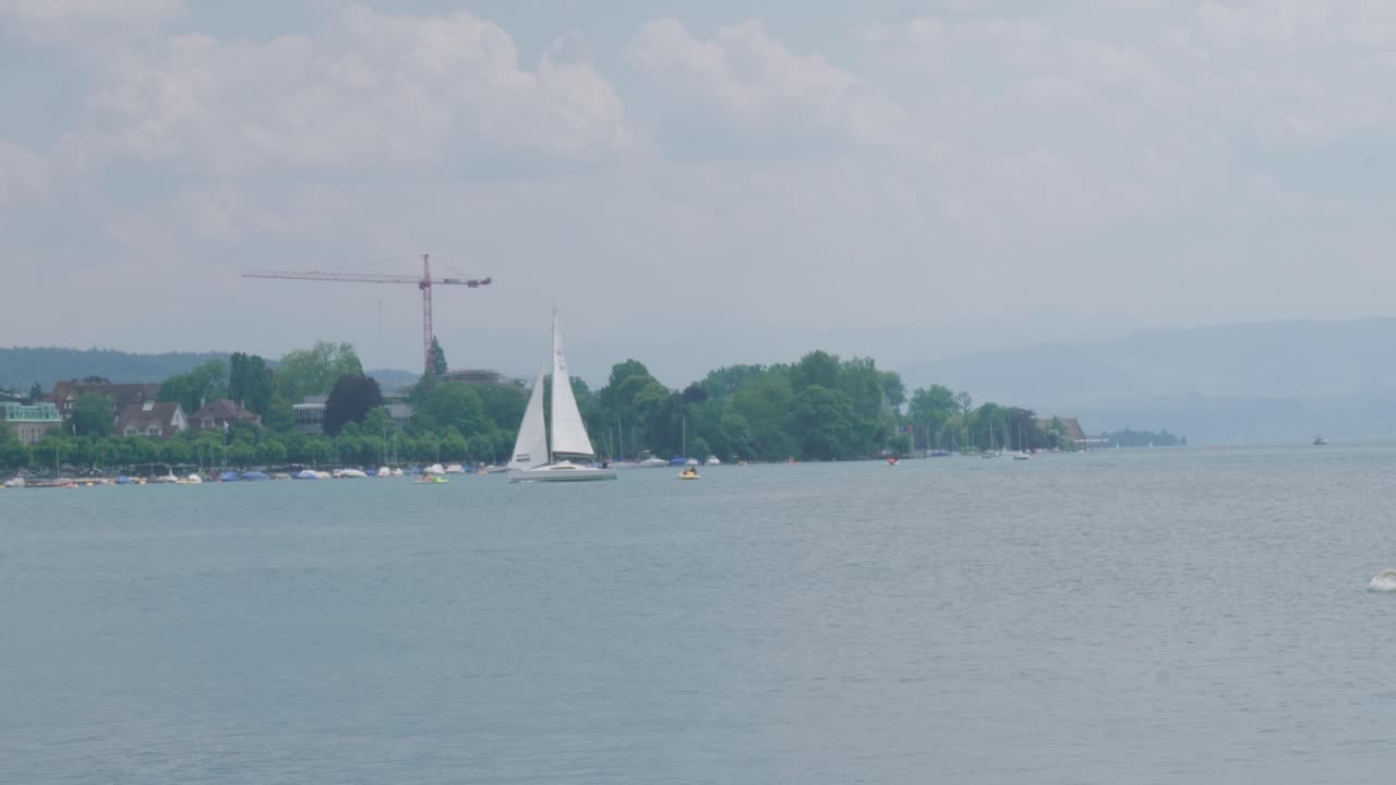 알프스 산맥  ⁇ 에 있는 아름다운 호수에서 스위스  ⁇ 발을 달고 항해하는 항해 보트의 풍경적인 드론 영상, 해안에 위치한 마을에서 멀지 않은