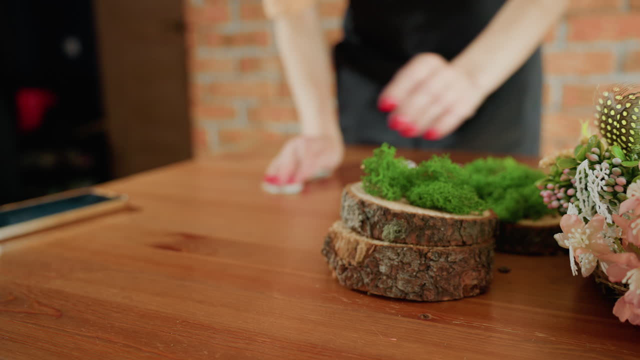 Closeup florist arranging colorful floral bouquet with pink berries, white blossoms, green leaves, dried flowers, rustic wood table, blurred background, creative handmade decoration, natural craft detail