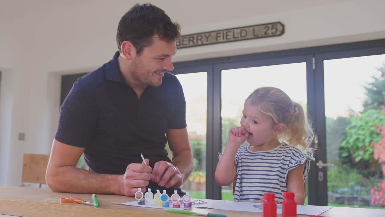 padre y hija joven divirtiéndose en casa sentados a la mesa y pintando la decoración juntos - filmado en cámara lenta