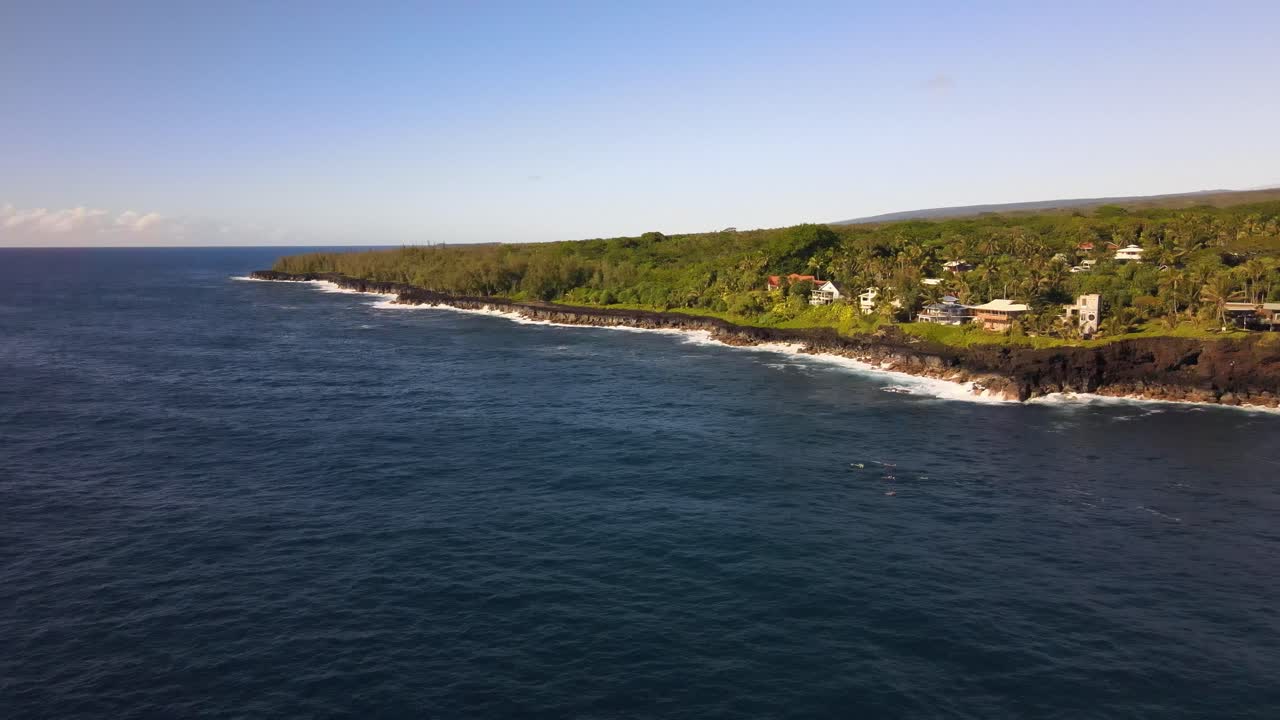 Riprese pomeridiane con drone rivelano case di Pahoa arroccate su scogliere mentre le onde del Pacifico si infrangono sotto, sotto cieli hawaiani sereni.