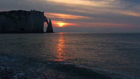 beautiful sunset behind mountain rock formation at ocean during evening. sunlight reflection in water. low angle wide shot.