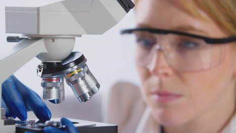 trabajadora de laboratorio que pone una diapositiva bajo el microscopio para su análisis