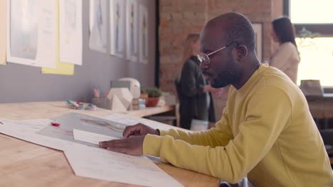 Side-View-Of-A-Focused-Man-Sitting-At-Drawing-Desk-And-Working-On-A-New-Project-In-An-Animation-Studio