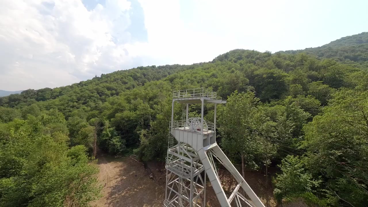 An aerial perspective of the historic Pozo de San Fernando coal mine buildings and headframe surrounded by lush green mountains in Aller, Asturias, Spain.