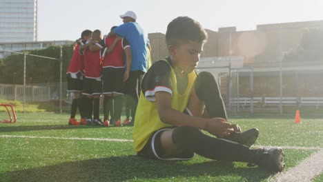 mixed race soccer kid lacing up his shoe in a sunny day