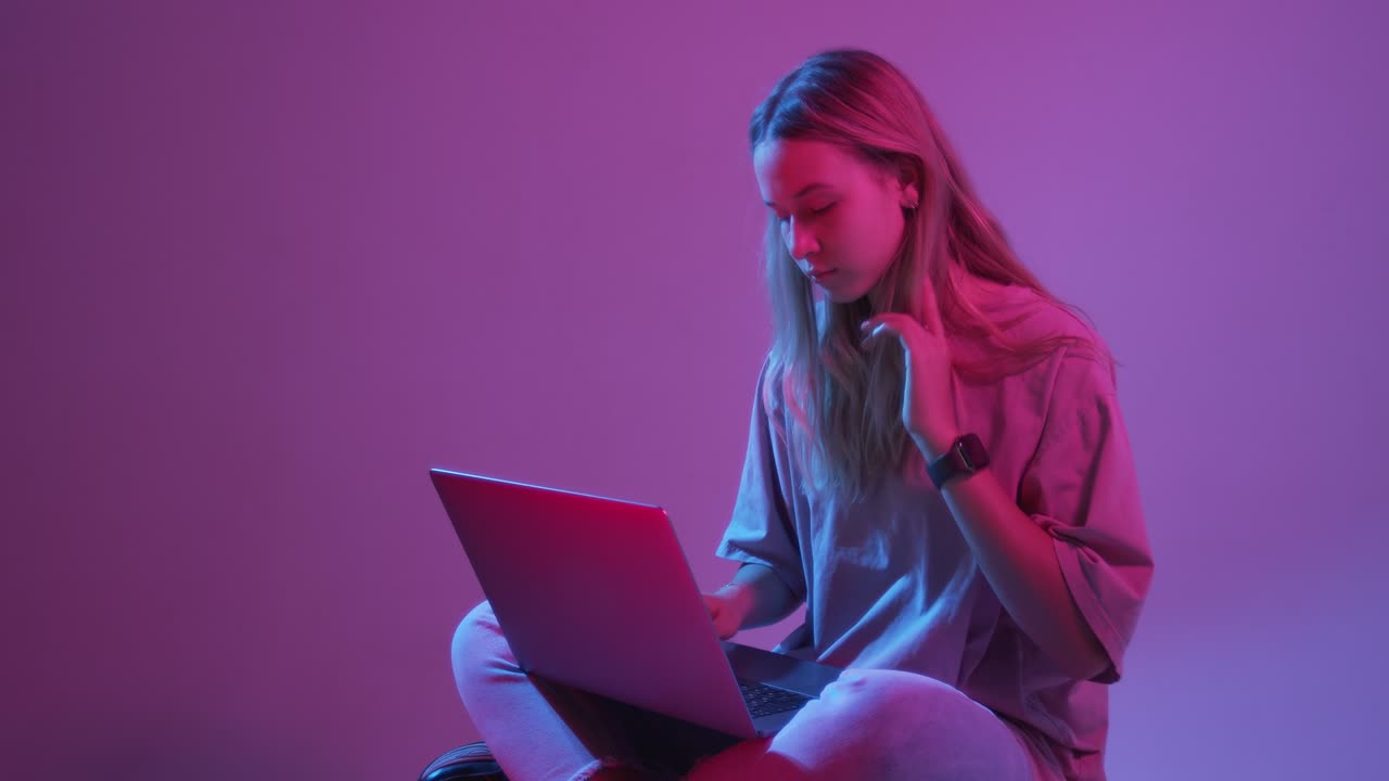 video en 4k de una joven blogger moderna con una computadora portátil, una tableta, una luz de neón de colores y un fondo