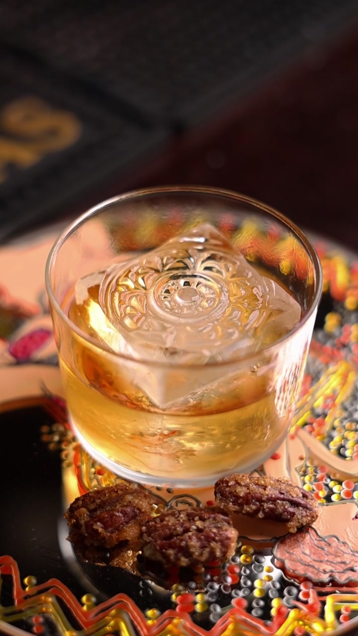 Bicchiere di whisky con cubetto di ghiaccio decorato e noci pecan candite
