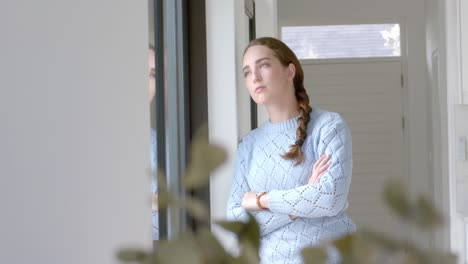 Portrait-of-thoughtful-caucasian-woman-with-arms-crossed-at-window-in-slow-motion