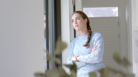 retrato de una mujer caucásica pensativa con los brazos cruzados en la ventana en cámara lenta