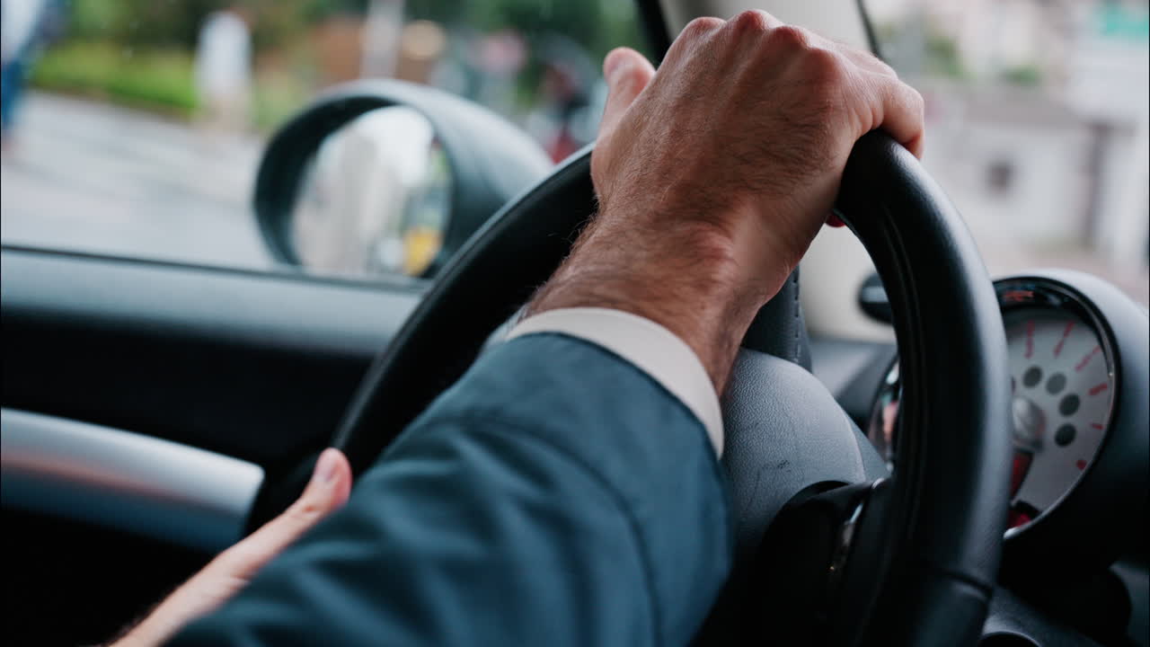 Close up of a man's hands on a steering wheel, driving a car on the road