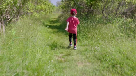 a moving shot of a cute kid in red t-shirt and cap playing in the beautiful forest