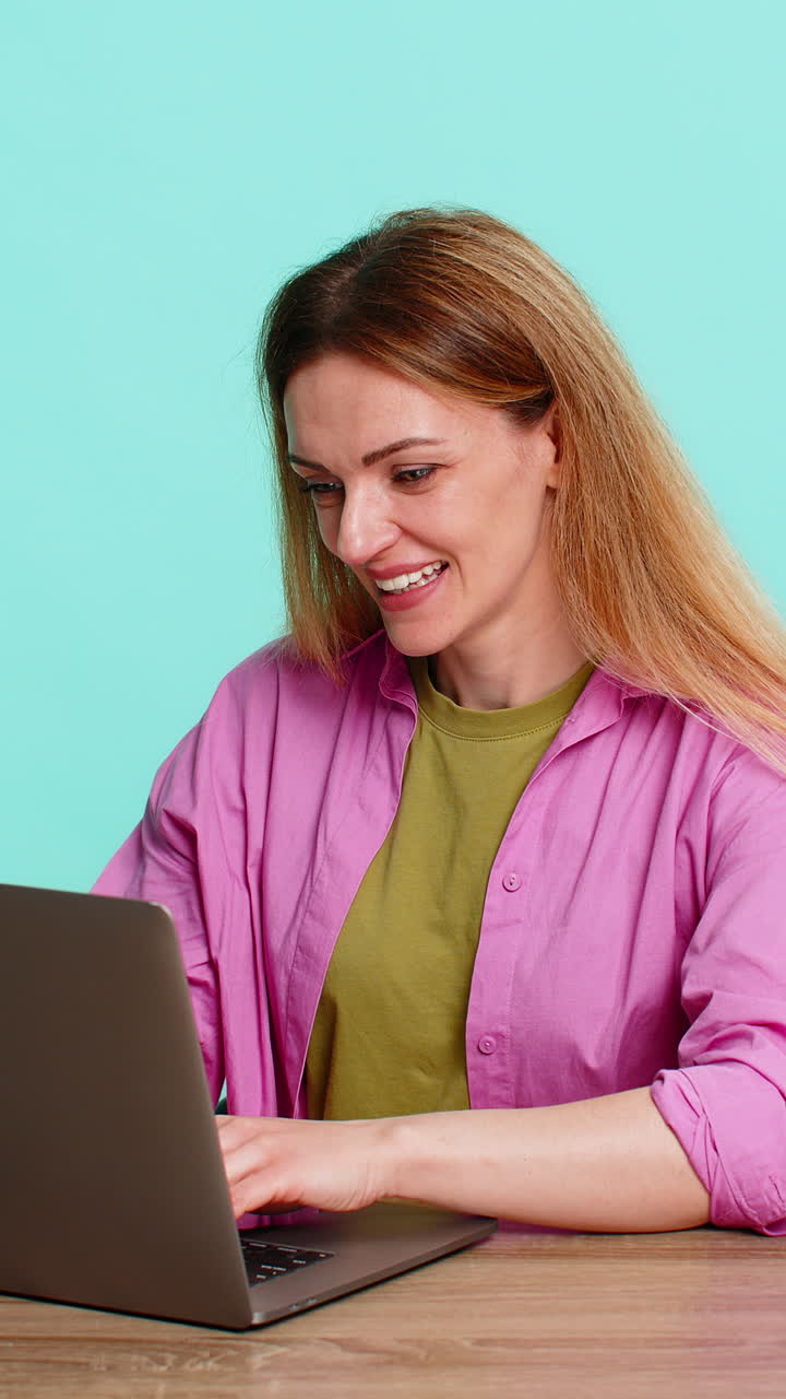 Woman sitting at table celebrating victory or success after receiving great news on laptop screen