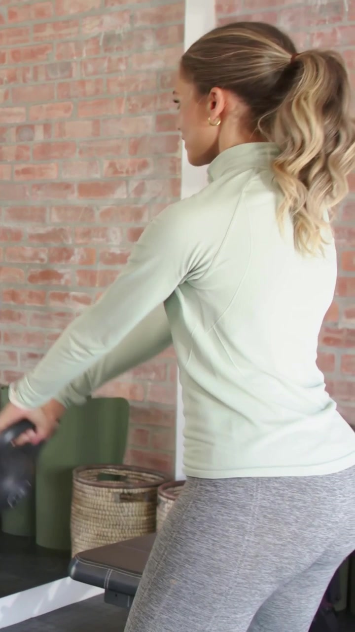 Video verticale: Donna con top verde e leggings che si allena con un kettlebell in palestra.