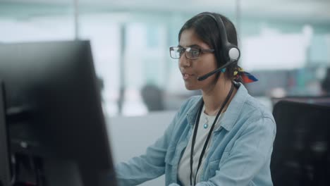 call center office: portrait of friendy indian female it customer support specialist working on computer. business entrepreneur using headset to talk with client via online video conference call