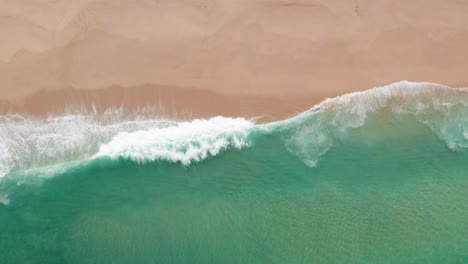 Top-down-view-of-waves-rolling-onto-sandy-beach-in-Portugal