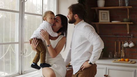 Young-mother-is-holding-her-cute-son-sitting-on-the-window-sill-together-with-young-father.-The-window-is-decorated-with