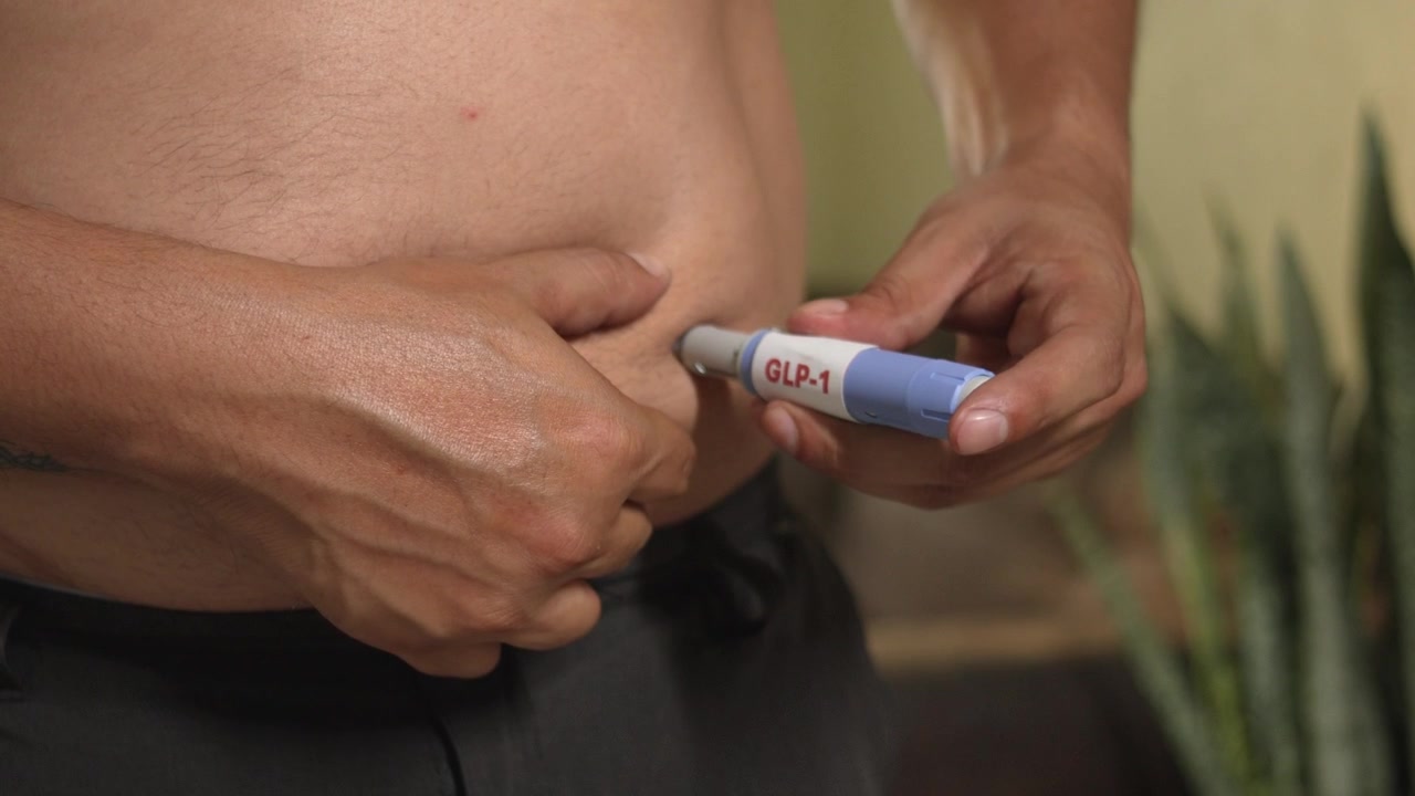 Uomo in sovrappeso che tiene una penna iniettore di GLP-1 (semaglutide) per la gestione del peso e la salute metabolica.