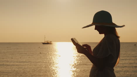 Silhouette-Einer-Jungen-Frau-Mit-Breitkrempigem-Hut,-Die-Ein-Tablet-Vor-Dem-Hintergrund-Einer-Schönheit-Benutzt