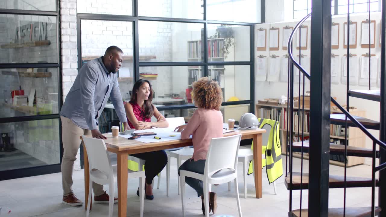 Diverse male and female architects having meeting and looking at blueprints at office, slow motion