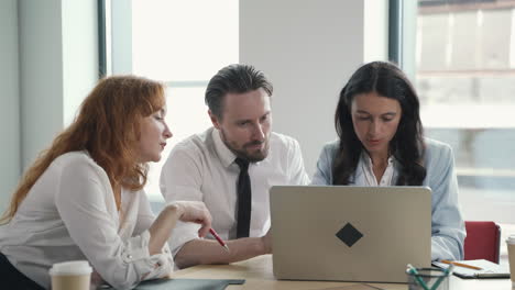 un joven equipo de trabajo compuesto por dos mujeres y un hombre consultando la computadora portátil juntos en una reunión de trabajo
