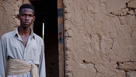 confident young villager standing at mud house entrance, embodying rural resilience and authentic cultural spirit of traditional african community life