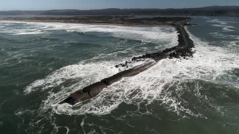 white foamy waves crash and roll across the coquille river jetty, aerial