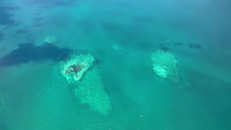 clear blue water revealing underwater rocks and coral formations from an aerial perspective