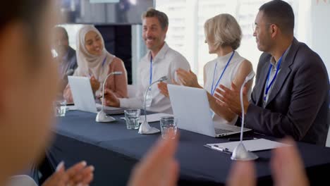 audience and panel of business delegates applauding businessman at a conference