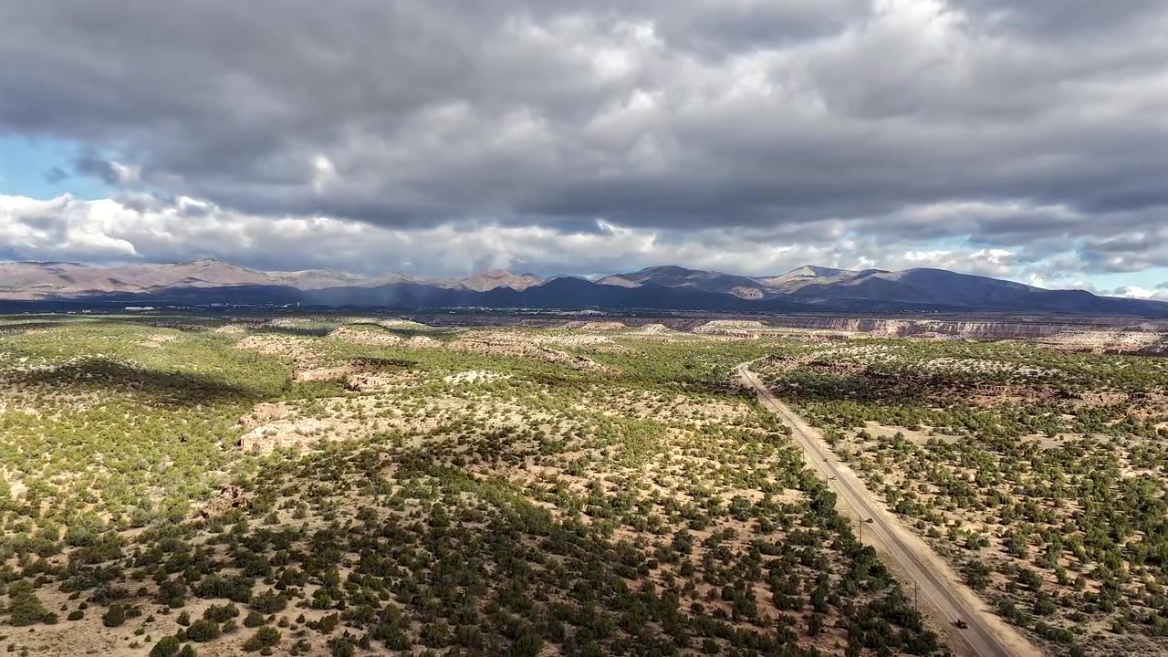 Un timelapse cinematografico con drone vola verso una cima montuosa tempestosa. Nuvole drammatiche in controluce e auto che guidano sulla strada sottostante creano un'atmosfera suggestiva ed epica del sud-ovest.