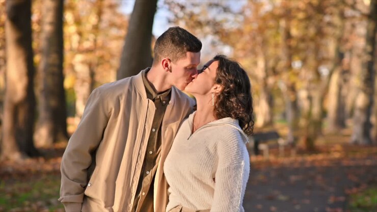 Um casal romântico em um parque no outono. Caminhando pelo caminho, abraçando e se beijando. Clima de outono, árvores e folhas amareladas ao redor. Câmera lenta