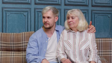 happy grown adult son laughing embracing talking to best friend older senior mother sit on sofa