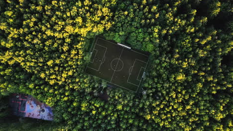 Aerial-screwdriver-shot-above-a-soccer-field-in-middle-of-sunlit-woodlands