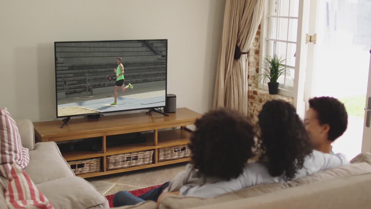 Composizione: famiglia felice seduta a casa insieme che guarda l'atletica del salto in lungo in TV.