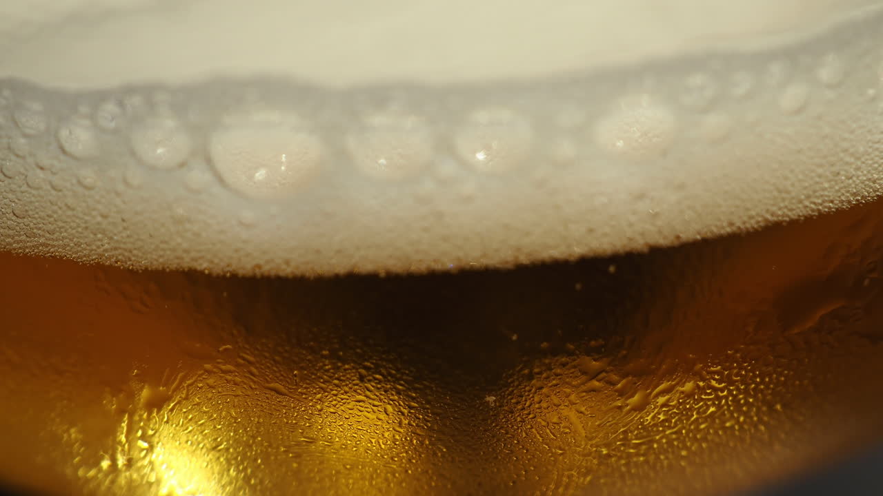 cabeza de cerveza espumosa bordeando la bebida dorada en una taza - primer plano extremo