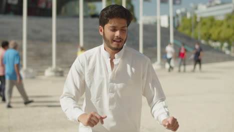 happy muslim man in white clothes dancing outside on sunny day.