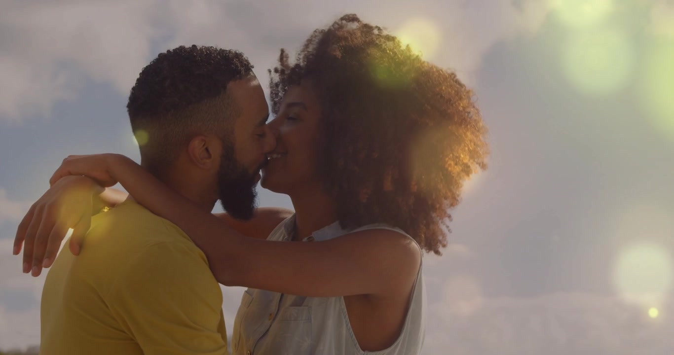 Couple embracing at shore gazing and leaning in tilting back with lens flare for romantic marketing