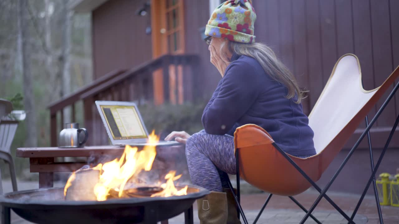 Woman working on laptop by fire pit outdoors