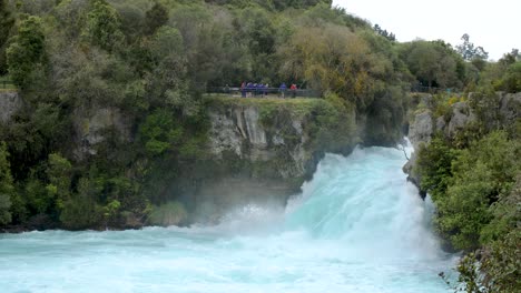 Establishing-shot-of-the-vibrant-blue-Huka-Falls-in-New-Zealand-with-tourists-off-in-the-distance