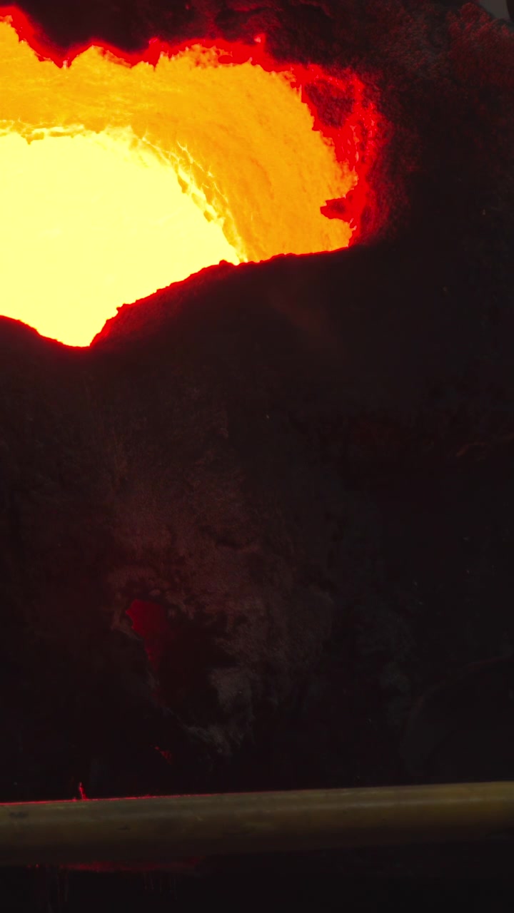 Intense close-up van gesmolten metaal dat uit een smeltkroes in een mal wordt gegoten, met een gloeiende oranje en witte kern die de duisternis verlicht.