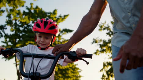 father teaches son to ride a bike on a sunny street