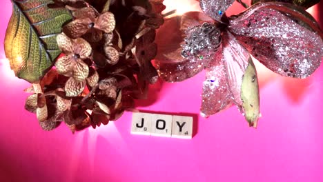 The-word-JOY-spelled-out-in-wooden-letters-on-a-pink-background-with-fairy-lights