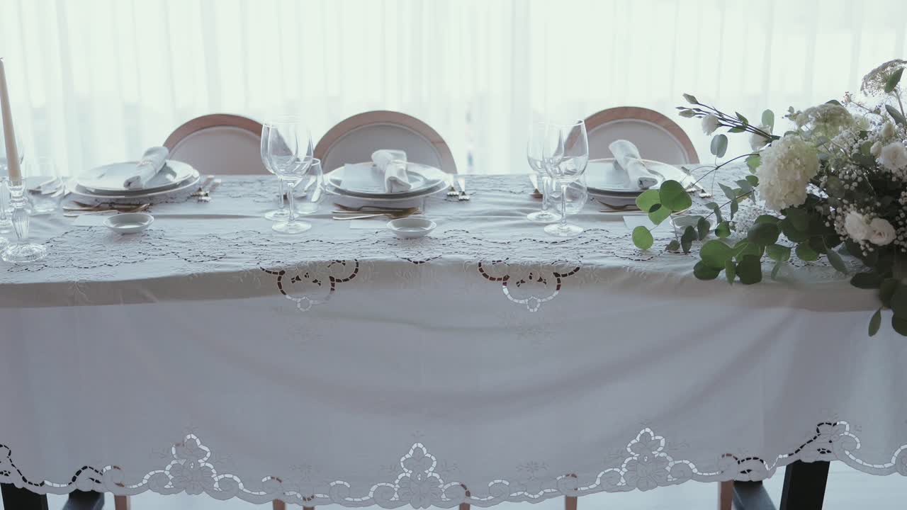 Mesa de boda luminosa con manteles blancos, platos, vasos y flores