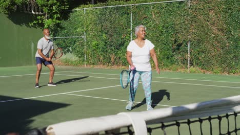 african american senior couple playing tennis on the tennis court on a bright sunny day