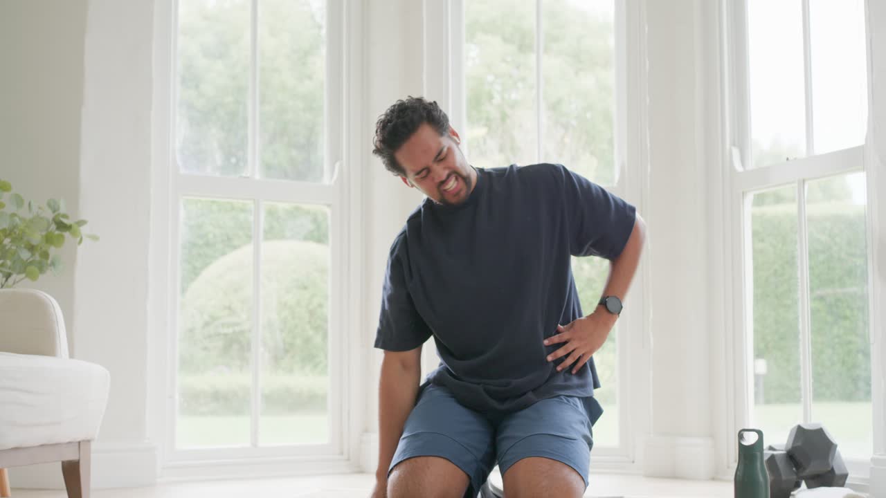 African American man exercising on mat at home, navy tee, shorts, checking side with tablet