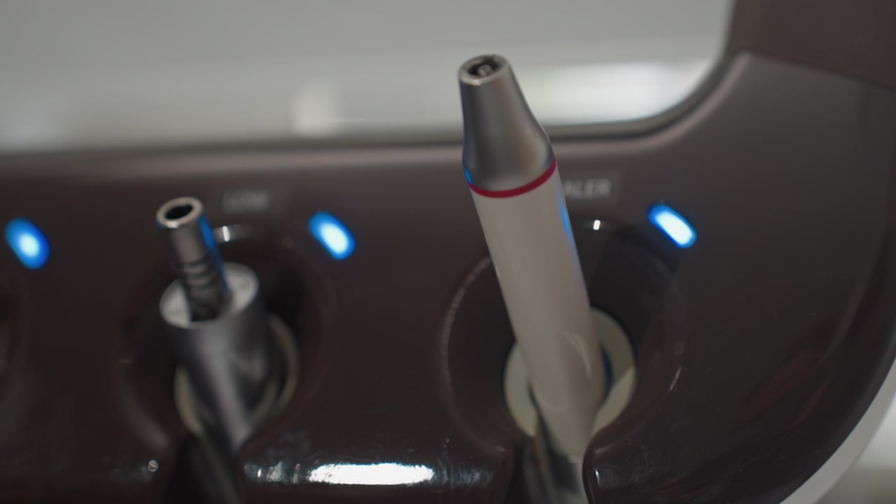 Close up of dental handpieces in docking station with blue indicator lights. instruments are stationary showcasing their metallic and plastic components against dark brown base. Soft