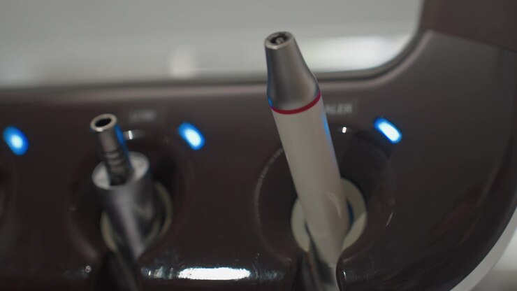 Close up of dental handpieces in docking station with blue indicator lights. instruments are stationary showcasing their metallic and plastic components against dark brown base. Soft